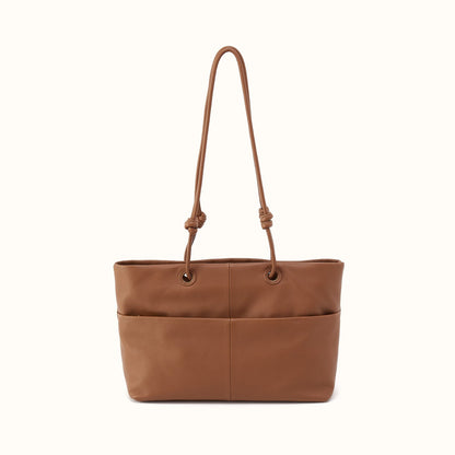A medium brown leather tote bag with a single shoulder strap featuring knotted details at the top, set against a plain off-white background.